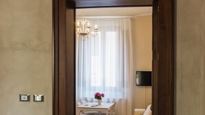A hallway with a wooden door leading to a dining area with a table and chairs, a sofa, and a TV mounted on the wall. - Alighieri Theatre charming suite (Ravenna)