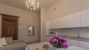 A modern kitchen with white cabinets, a sink, and a dining area with a table set for breakfast. - Alighieri Theatre charming suite (Ravenna)