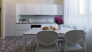A modern kitchen with white cabinets, a dining table with two chairs, and a potted plant. - Alighieri Theatre charming suite (Ravenna)