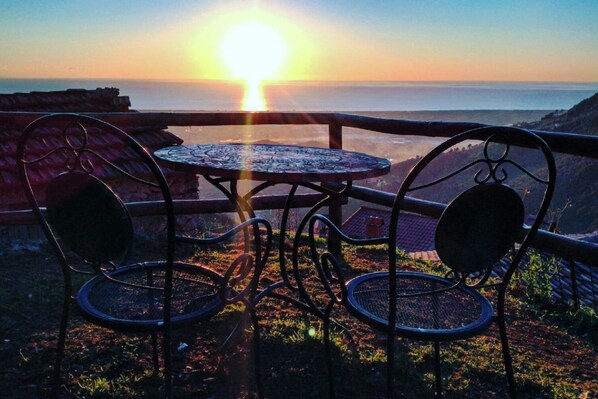 A sunset view from a terrace with a table and chairs.