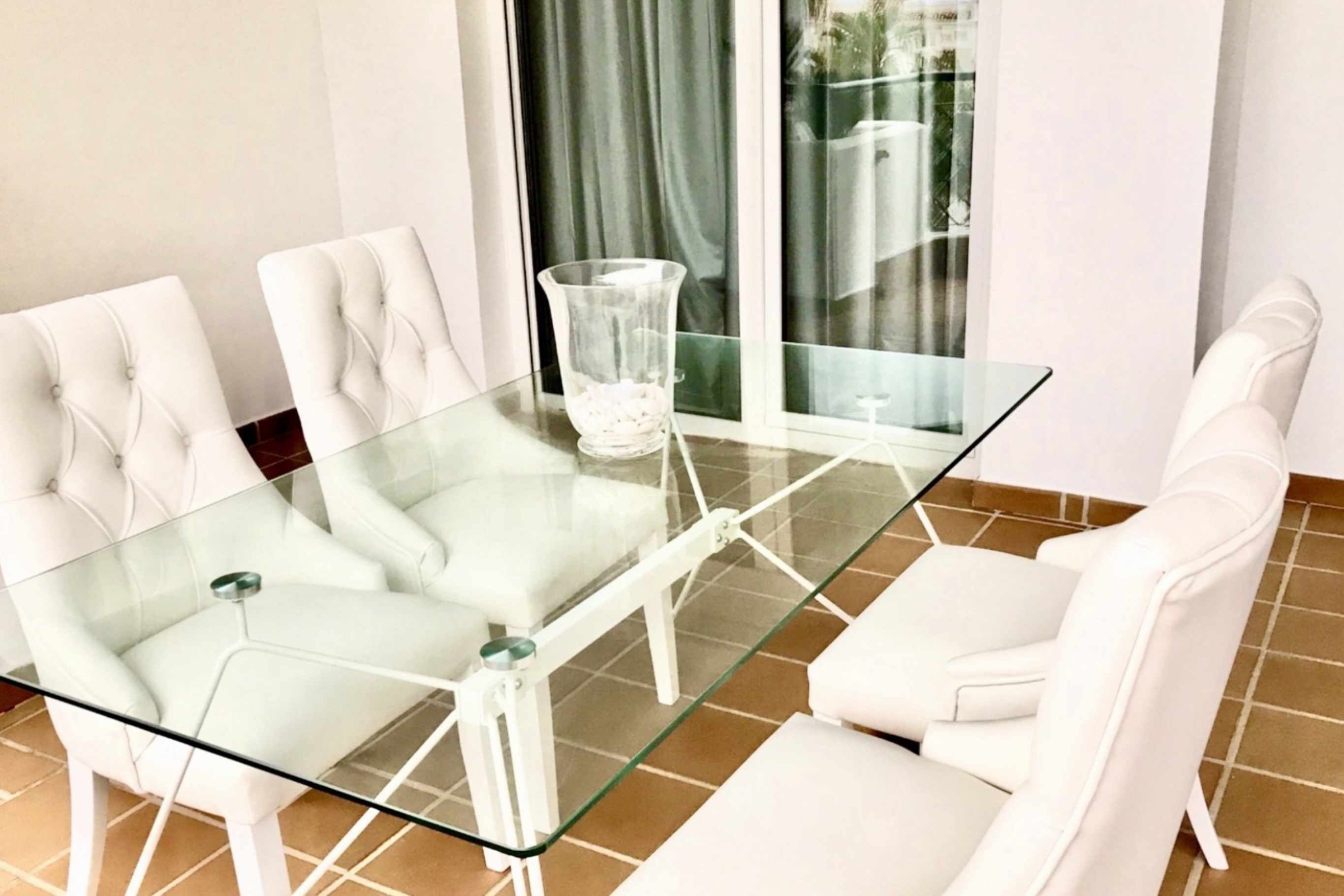Et moderne spiseområde med et glasbord og hvide polstrede stole.