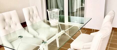 Et moderne spiseområde med et glasbord og hvide polstrede stole.