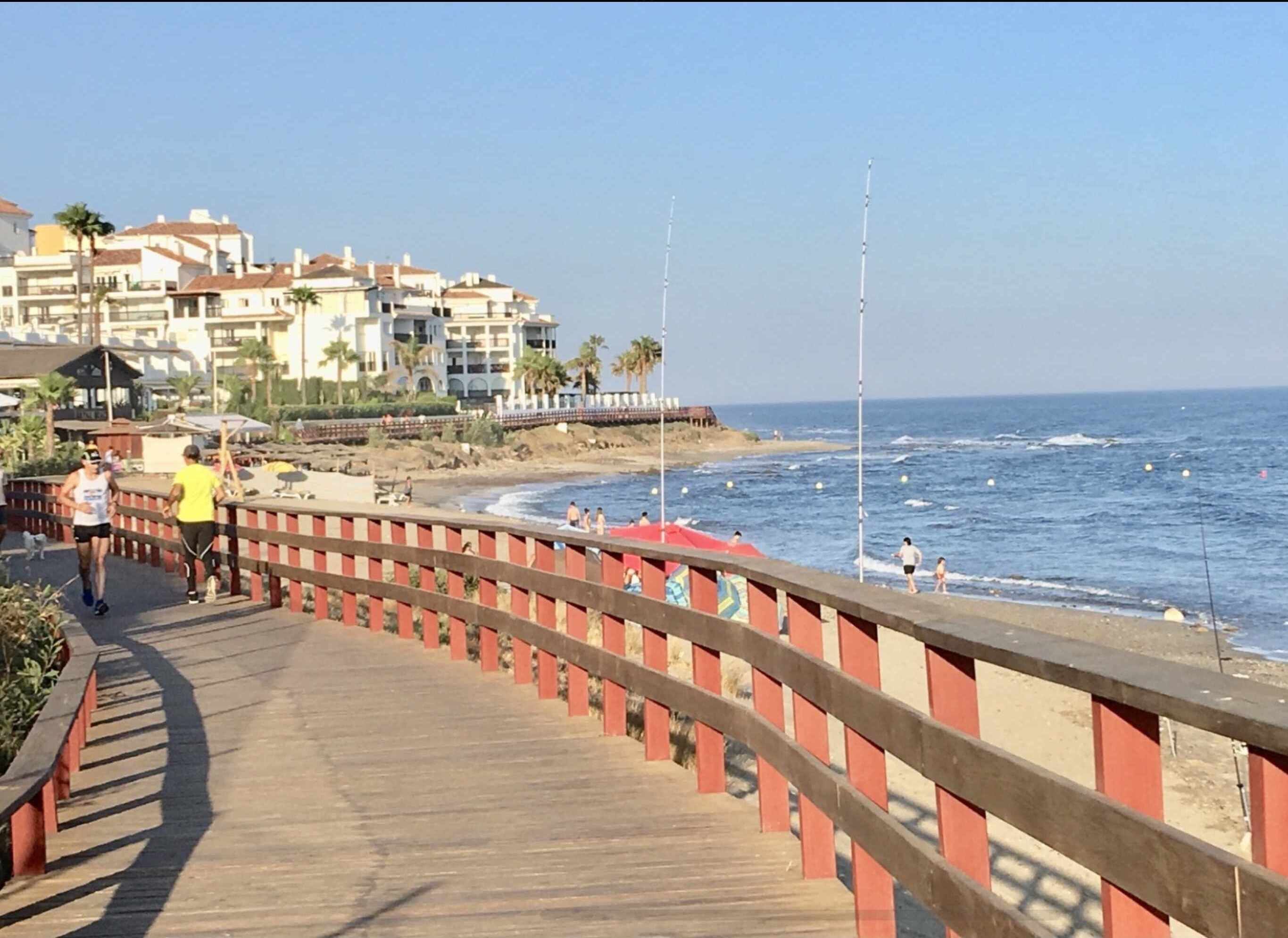 A wooden boardwalk with red railings leading to a beach.