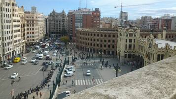Una concurrida calle urbana con edificios históricos, una plaza central y una alta torre con reloj.