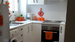 Een kleine keuken met witte kastjes, een wasmachine en een klein oven.