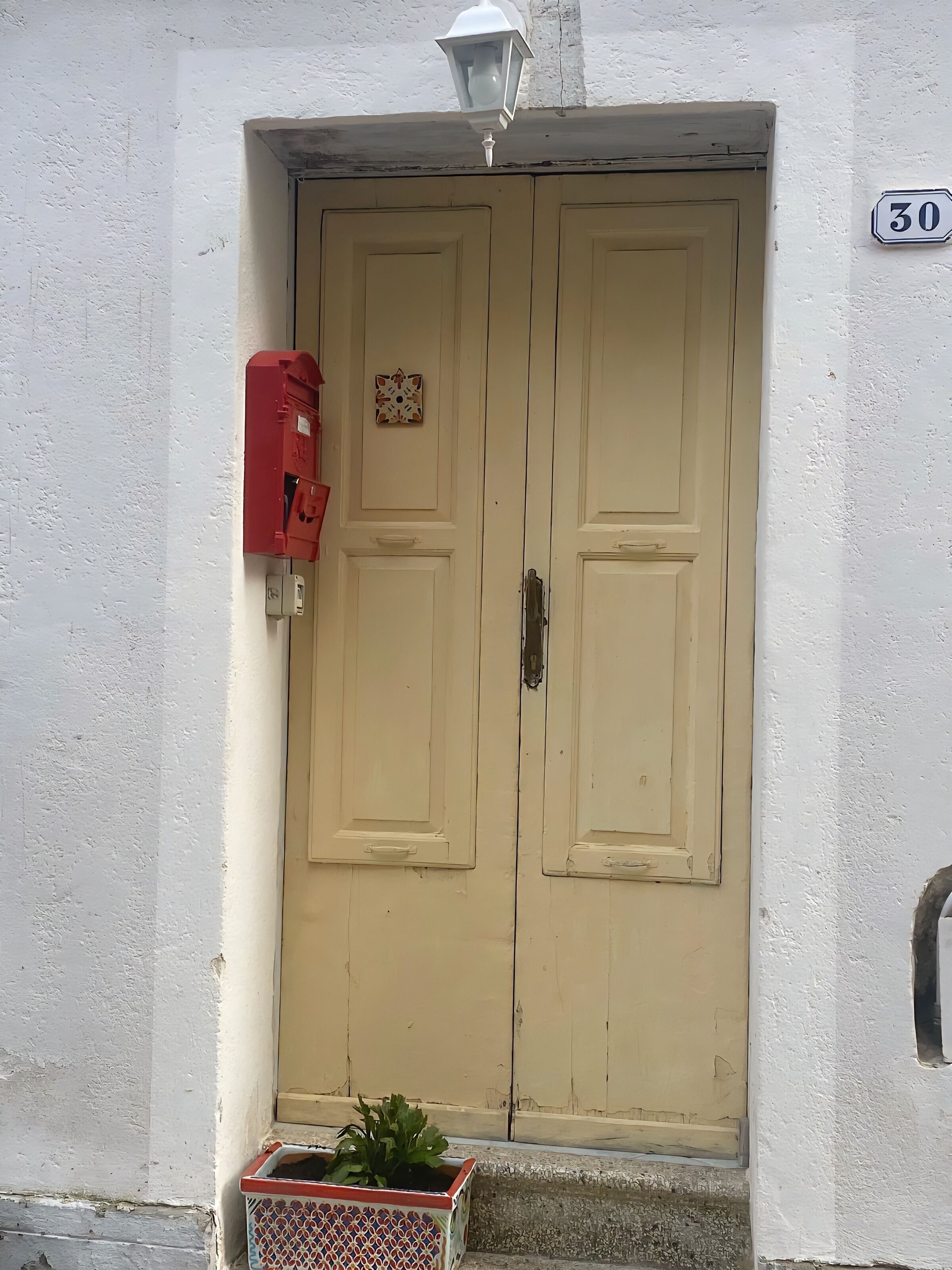 A double door with a number '30' sign above it, a red fire alarm box, and a patterned planter at the entrance.