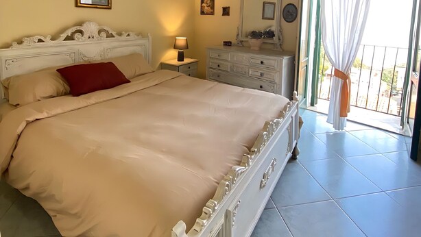 A bedroom with a bed, a dresser, a nightstand, a mirror, and a window with curtains.