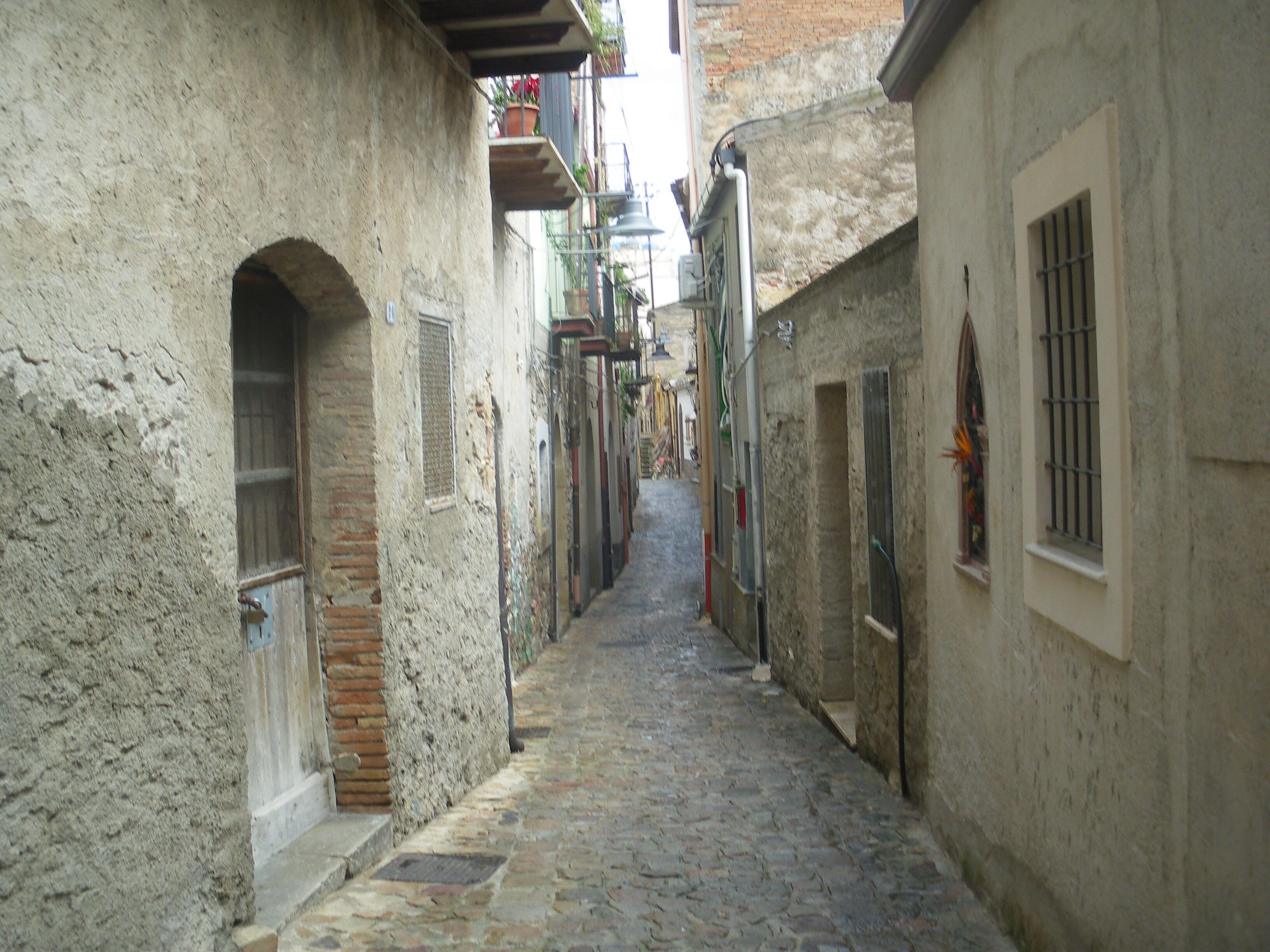 Une étroite ruelle pavée, située entre des bâtiments aux murs de pierre et aux portes en arc de cercle.