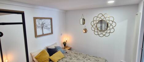 A bedroom with a bed, a nightstand, a wall-mounted mirror, and a framed picture.
