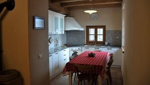 Une cuisine de taille réduite avec des meubles blancs, une cuisinière et une table recouverte d’une nappe rouge.