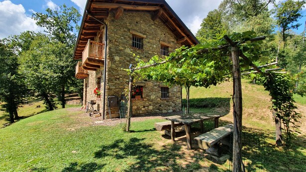 Une maison en pierre avec un toit en pente, un balcon en bois et un petit jardin agrémenté d’une table et d’un banc.