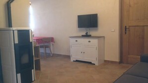 Une pièce avec un sol carrelé, un meuble blanc avec des tiroirs, un téléviseur posé sur le dessus, et une porte à l’arrière-plan.