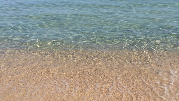 Une plage avec une eau claire et peu profonde, et un bateau visible au loin.
