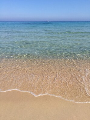 Una spiaggia con acque limpide e poco profonde e una barca in lontananza.