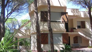 Un immeuble à plusieurs étages doté d’un balcon, entouré d’arbres et de plantes en pot.