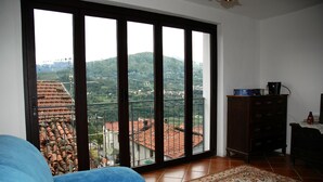 Ein Zimmer mit einer großen Schiebetür, die auf einen Balkon mit Blick auf eine hügelige Landschaft führt.