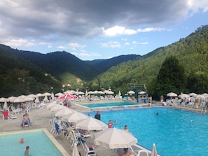 Ein Poolbereich mit mehreren Schwimmbecken, Liegestühlen und Sonnenschirmen.