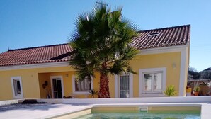 Une piscine à l’eau claire, un palmier et un bâtiment jaune avec un toit en tuiles.