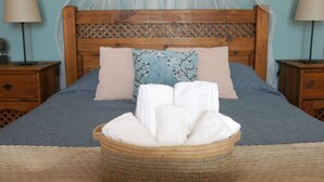 Un lit bien fait, avec une couette bleue, une tête de lit en bois et un panier en osier rempli de serviettes blanches.