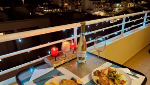 Een balkon met een tafeltje, een fles wijn, kaarsen en borden eten.