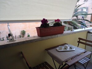 Un balcón con una mesa, sillas, una planta en maceta y vistas a un edificio y palmeras.