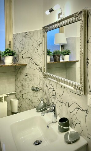 Un baño con pared de mármol, un espejo grande y un lavamanos con grifo moderno.