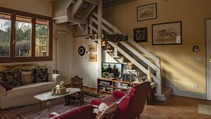 Ett mysigt vardagsrum med en soffa, en röd fåtölj och ett soffbord. En trappa med ett dekorativt räcke leder upp till en övre våning.