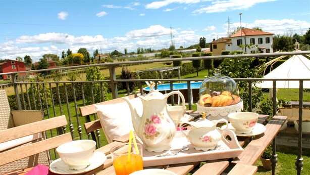 Una terrazza con area pranzo, dotata di tavolo, sedie e vista su una piscina e case sullo sfondo.