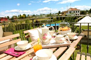 Eine Terrasse mit Essbereich, inklusive Tisch, Stühlen und Blick auf einen Swimmingpool sowie Häuser im Hintergrund.