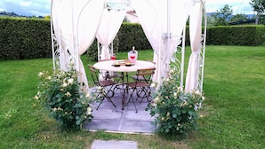 Un gazebo in giardino con un tavolo rotondo e sedie, circondato da cespugli di rose.