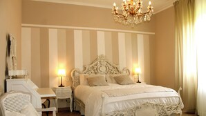 Un'elegante camera da letto con un letto grande e decorato, due comodini con lampade, una sedia bianca e un lampadario.