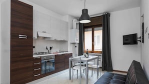Une cuisine moderne avec des meubles de couleur bois foncé, un coin repas comprenant une table et des chaises, et un canapé en cuir noir.