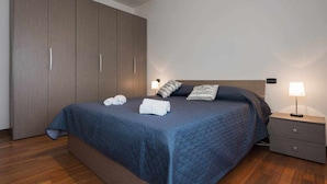 Une chambre à coucher avec un grand lit, une armoire, une table de chevet avec une lampe et une commode.