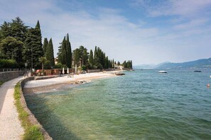 A coastal walkway with a sandy beach, trees, and a clear view of the sea.