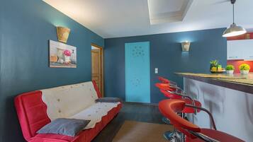 A modern living room with a red sofa, a kitchen area with bar stools, and a blue accent wall.