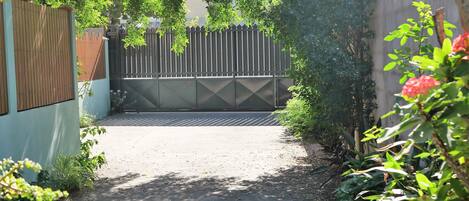 Una entrada protegida con reja metálica, rodeada de abundante vegetación y un camino de hormigón.