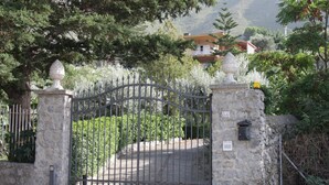 A gated entrance with a stone wall, a metal gate, and a stone pillar with a number plaque.