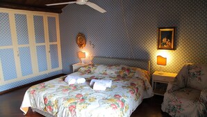 Ett sovrum med ett blommigt sängöverkast, två sänglampor, en takfläkt och en inramad tavla på väggen.