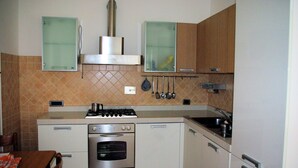 Eine kompakte Küche mit Gasherd, Backofen und Spüle. Es befinden sich Küchenutensilien an der Wand und über der Spüle ein kleines Fenster.