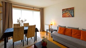 Een woonkamer met een eettafel, stoelen, een bank, een lamp en een schilderij aan de muur.