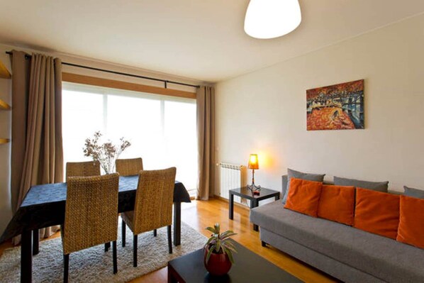 A living room with a dining table, chairs, a sofa, a lamp, and a painting on the wall.