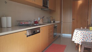Een moderne keuken met houten kastjes, een RVS spoelbak en een eethoek met een tafelkleed met stippen.