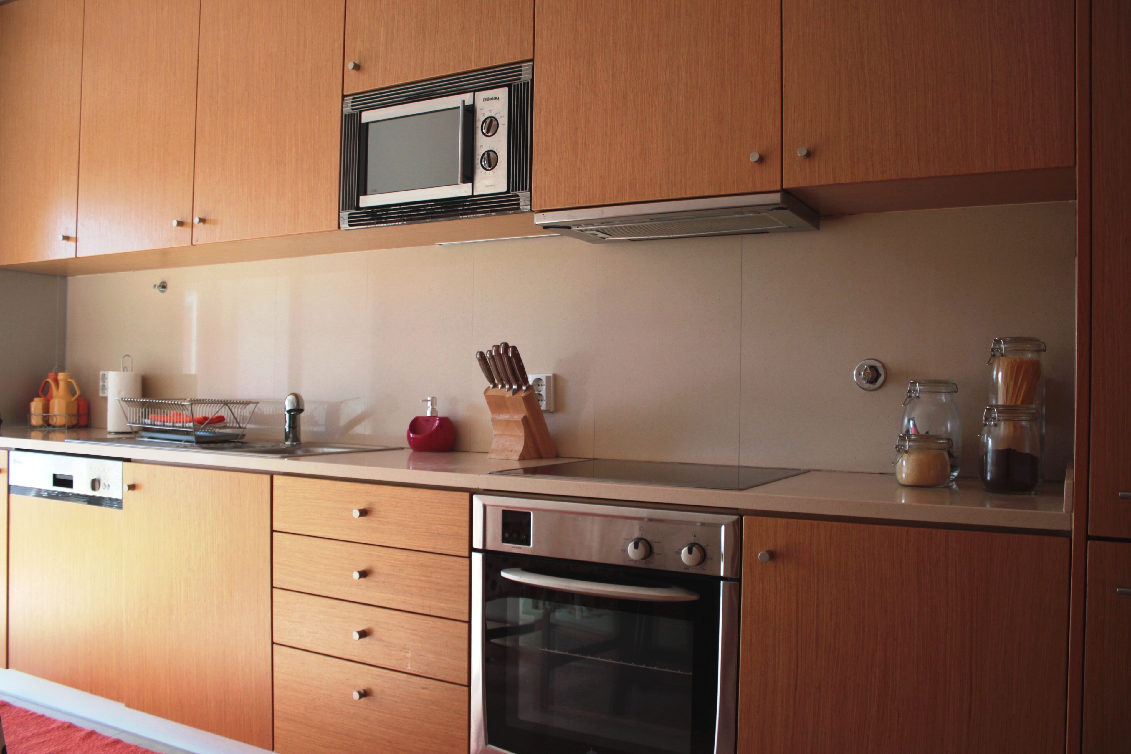 A kitchen with wooden cabinets, a microwave, a stove, and various kitchen items on the countertop.