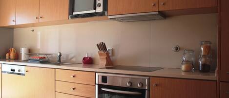 A kitchen with wooden cabinets, a microwave, a stove, and various kitchen items on the countertop.