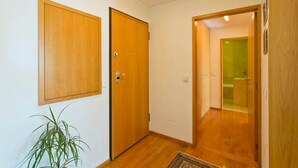Een gang met houten deuren, een plant in pot en een zichtbare badkamer door een geopende deur.