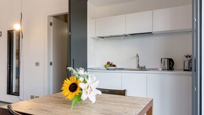 A dining table with a vase of flowers, a wooden chair, and a kitchen in the background. - Studio Vaticano Int. 5B - Terrace with View on San Pietro (Roma)
