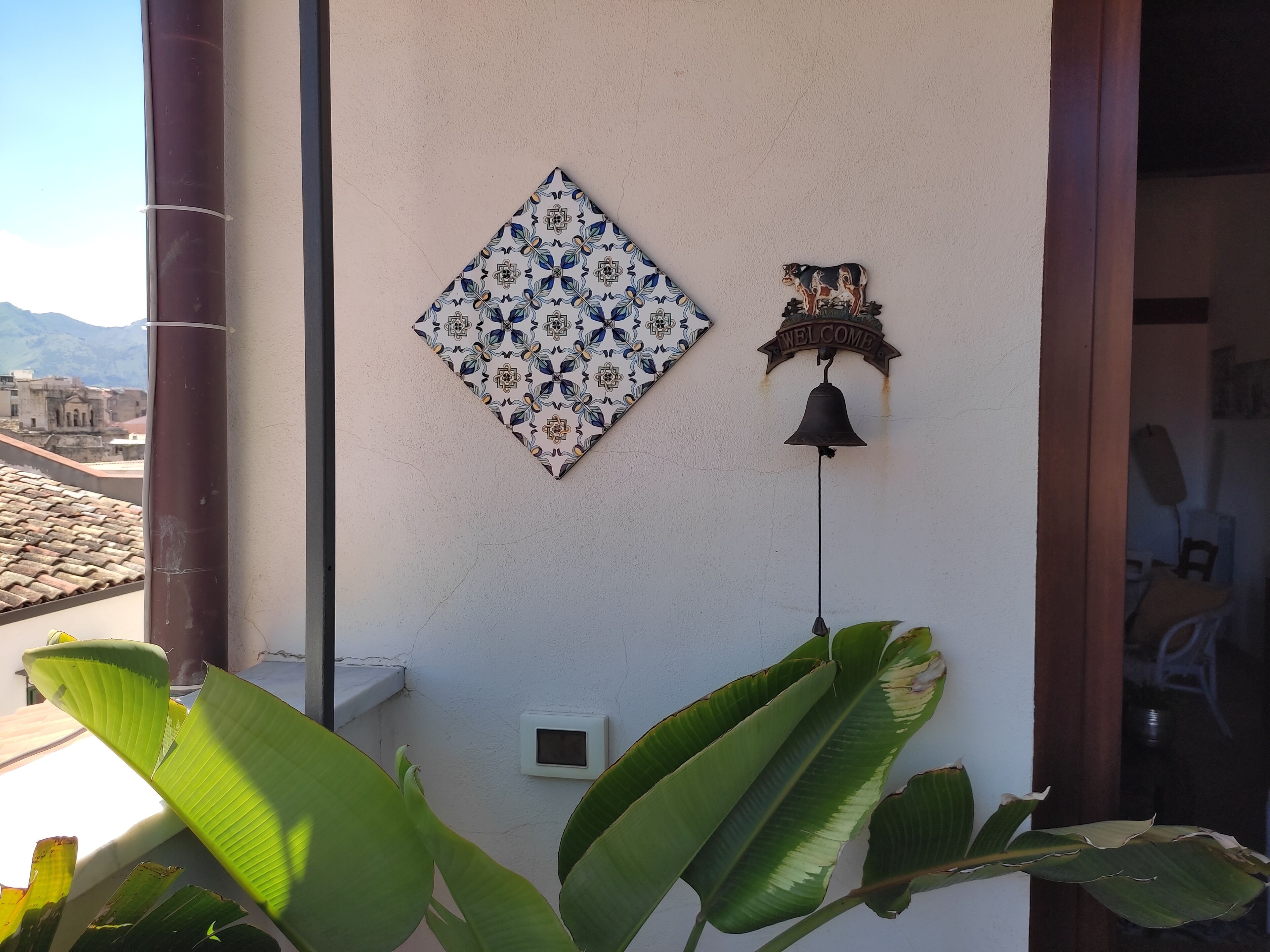 A wall with a decorative tile, a welcome bell, and a thermostat.