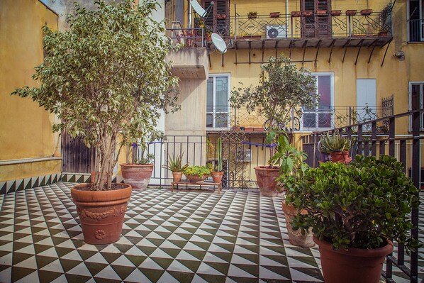 A courtyard with a checkered floor, potted plants, and a building with balconies.