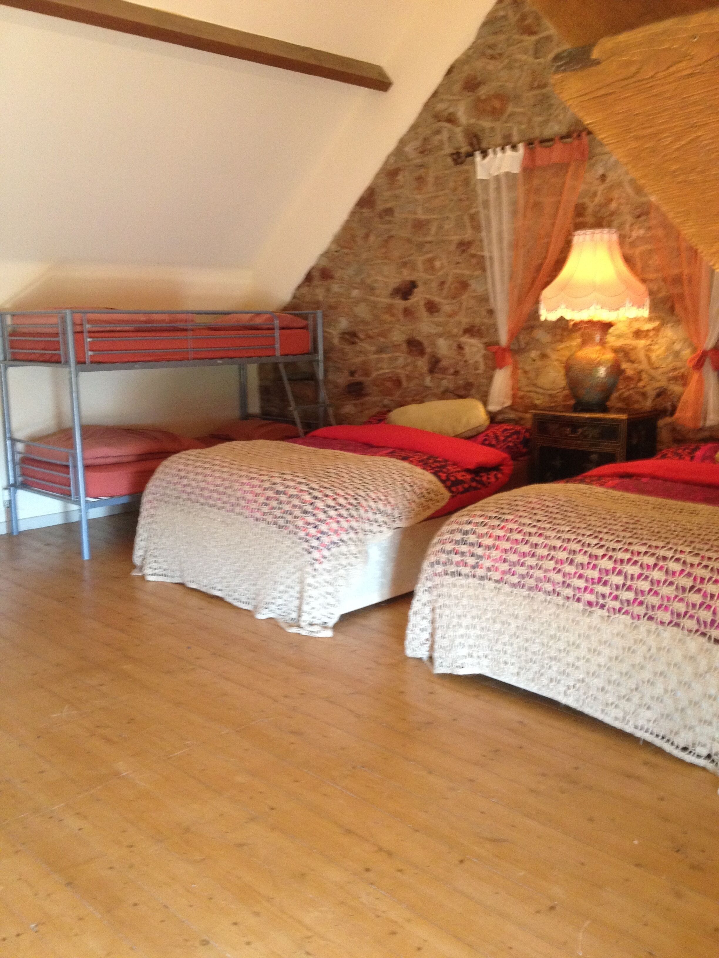 A cozy room with a stone wall, a wooden ceiling, and a bunk bed with red bedding.