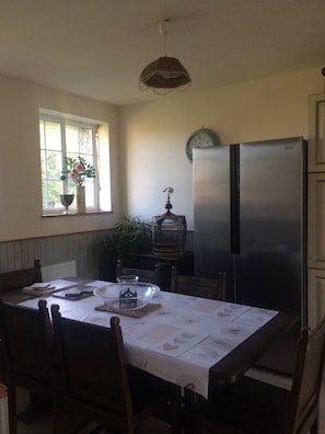 Ein Essbereich mit einem Tisch für zwei Personen, einer Wanduhr und einem Kühlschrank.